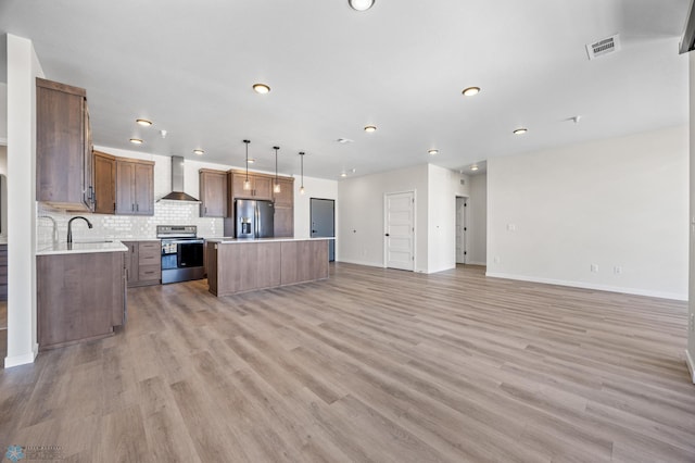 kitchen featuring a kitchen island, light countertops, open floor plan, stainless steel appliances, and wall chimney exhaust hood