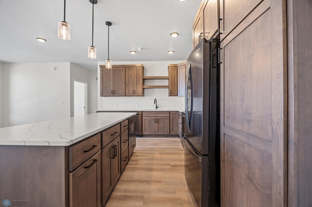 kitchen with open shelves, a barn door, light wood-style flooring, freestanding refrigerator, and decorative backsplash