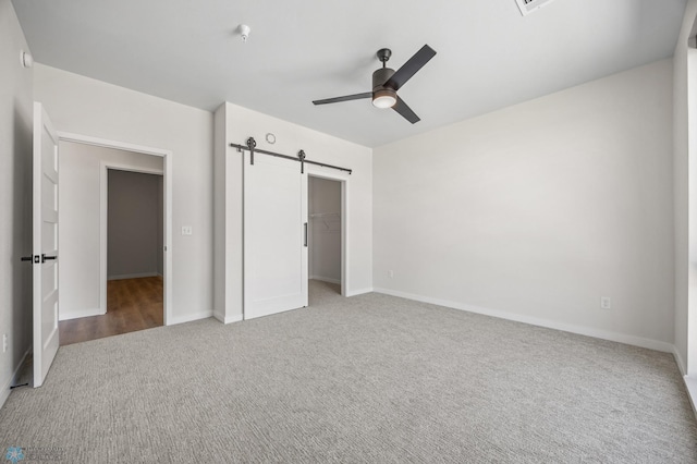 unfurnished bedroom with a closet, baseboards, a barn door, a ceiling fan, and carpet