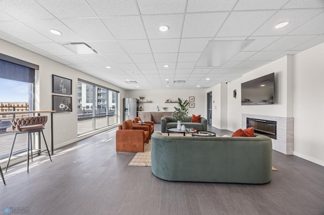 living room with visible vents, wood finished floors, baseboards, a paneled ceiling, and a tile fireplace