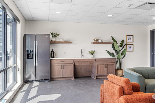 interior space with open shelves, a drop ceiling, a wealth of natural light, and stainless steel fridge with ice dispenser