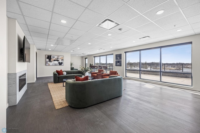 living area with a fireplace, baseboards, a drop ceiling, and dark wood-type flooring