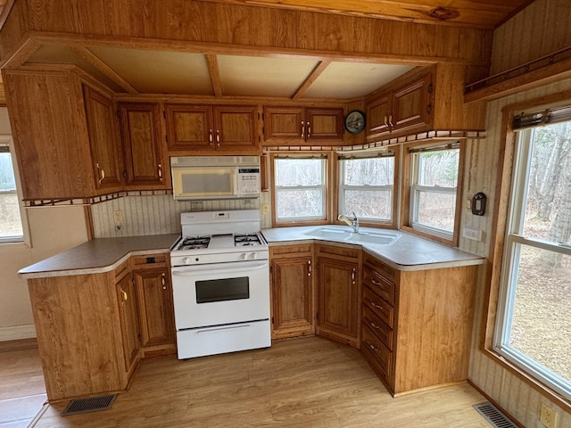 kitchen featuring a sink, light wood-style floors, white appliances, brown cabinetry, and visible vents