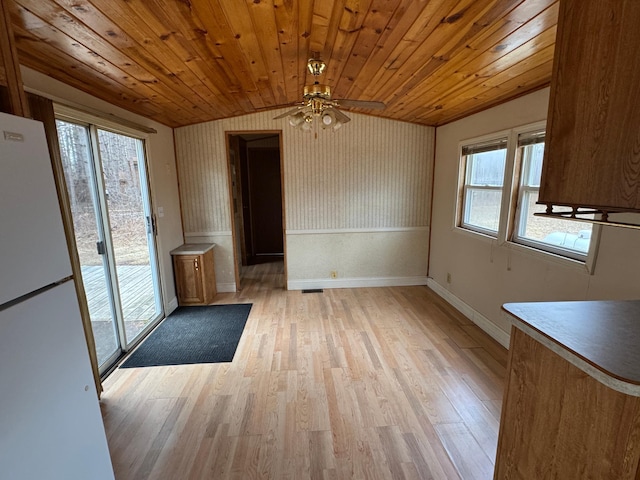 unfurnished dining area featuring baseboards, a ceiling fan, light wood-style flooring, and wood ceiling