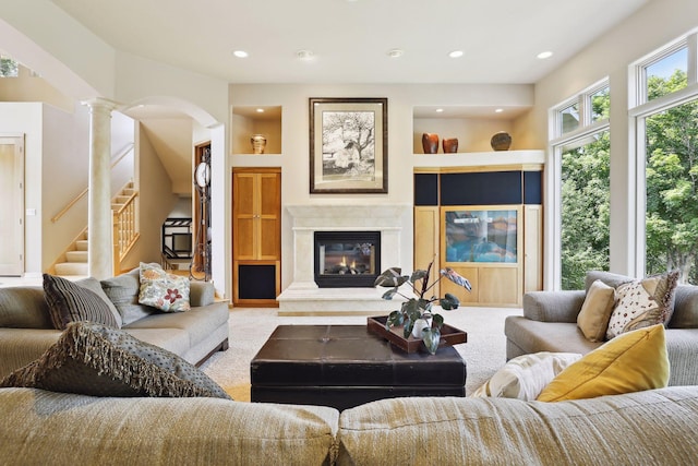living room featuring carpet floors, arched walkways, decorative columns, and a glass covered fireplace