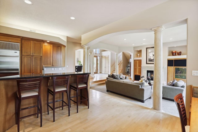 kitchen featuring brown cabinetry, a breakfast bar area, ornate columns, stainless steel built in fridge, and arched walkways
