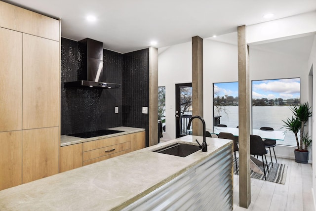 kitchen with a sink, black electric cooktop, modern cabinets, and wall chimney range hood