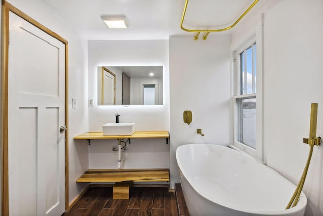 full bathroom with baseboards, a sink, a freestanding bath, and wood finished floors