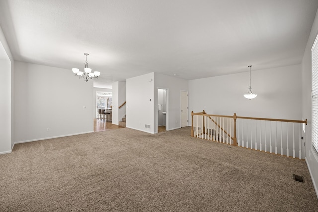 carpeted empty room featuring visible vents, baseboards, and a chandelier