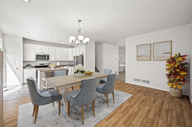 dining area with a notable chandelier, light wood finished floors, recessed lighting, visible vents, and stairway