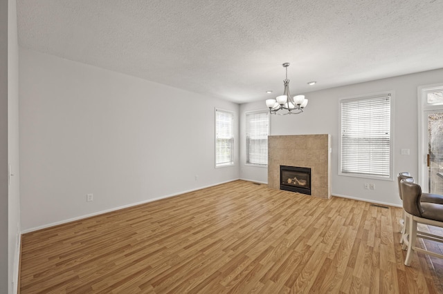 unfurnished living room with a textured ceiling, a notable chandelier, baseboards, and light wood-type flooring