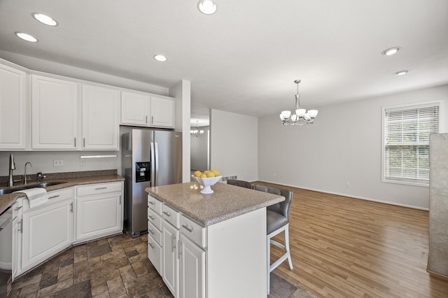 kitchen with a notable chandelier, a sink, stainless steel appliances, white cabinetry, and a kitchen bar