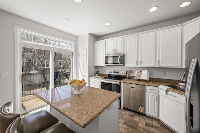 kitchen with appliances with stainless steel finishes, a sink, a center island, white cabinetry, and stone finish flooring
