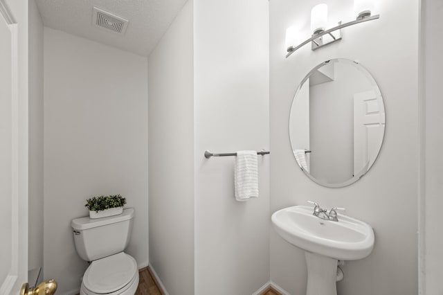 bathroom featuring a textured ceiling, visible vents, a sink, baseboards, and toilet