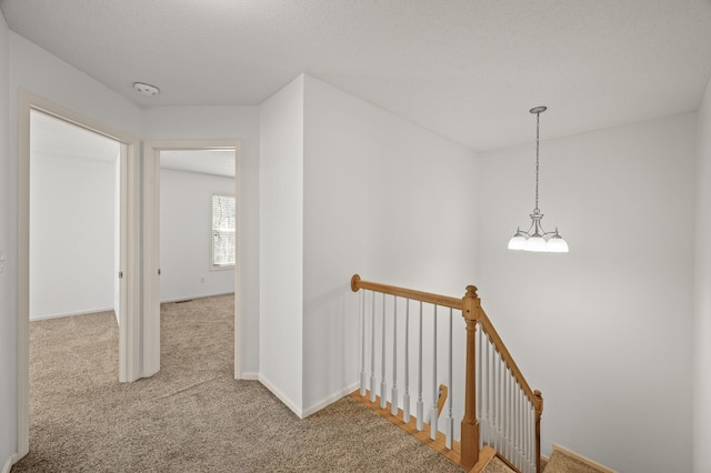 hall featuring a notable chandelier, carpet flooring, and an upstairs landing