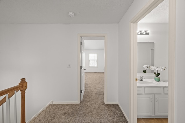hallway featuring baseboards, a sink, an upstairs landing, and light carpet