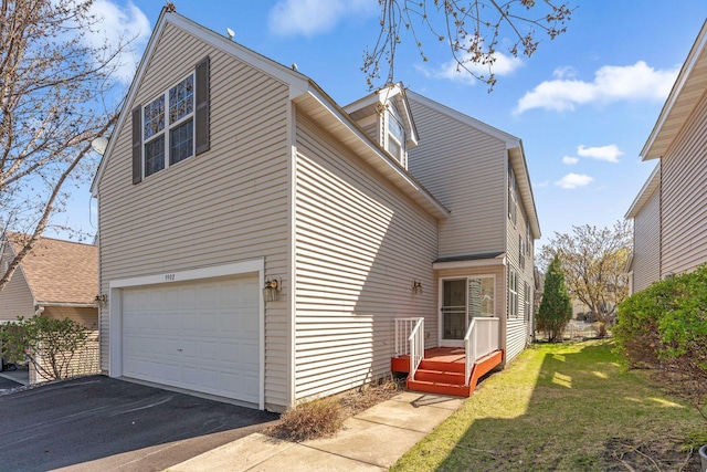 view of side of home featuring an attached garage, a yard, and aphalt driveway