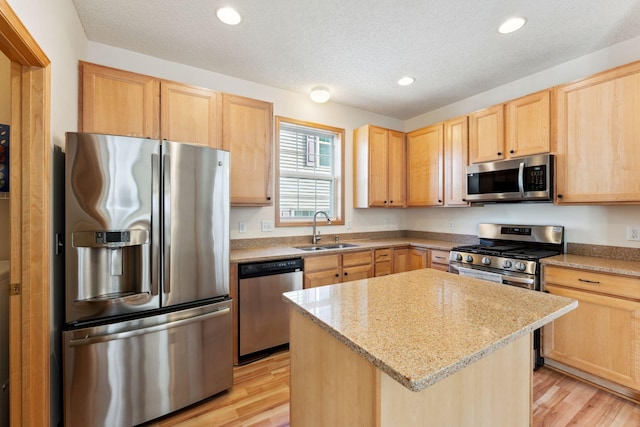 kitchen featuring a textured ceiling, a sink, light wood-style floors, light brown cabinets, and stainless steel appliances