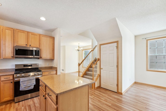kitchen with an inviting chandelier, light wood finished floors, light stone counters, and stainless steel appliances