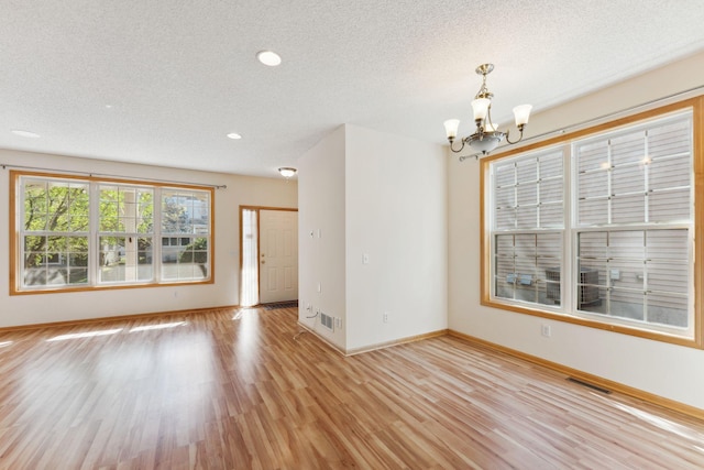 unfurnished dining area featuring a textured ceiling, an inviting chandelier, baseboards, and light wood-style floors