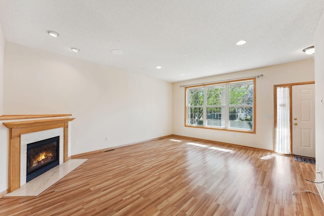 unfurnished living room featuring a high end fireplace, baseboards, recessed lighting, and light wood-type flooring