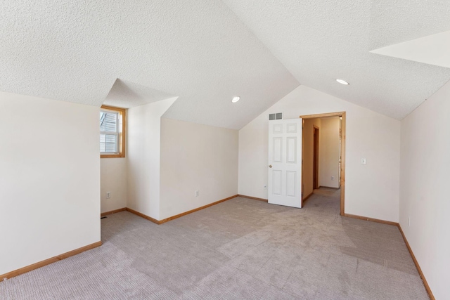 additional living space with a textured ceiling, visible vents, light carpet, and vaulted ceiling