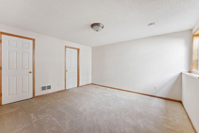 carpeted empty room featuring a textured ceiling, visible vents, and baseboards