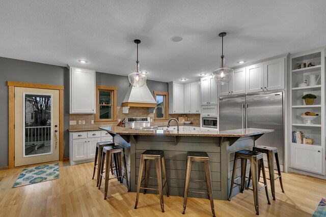 912 21st Ave N, Sartell, MN 56377 - kitchen featuring white cabinets, light wood finished floors, built in appliances, premium range hood, and decorative backsplash