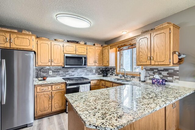 kitchen featuring a sink, stainless steel appliances, a peninsula, and a textured ceiling