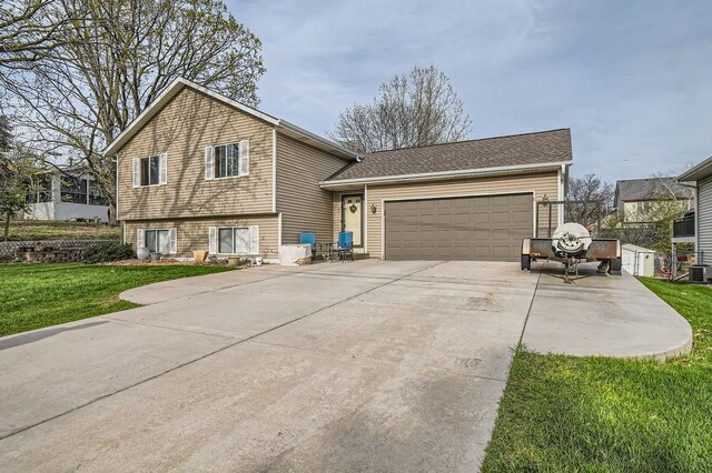 split level home featuring an attached garage, concrete driveway, central AC, and a front yard
