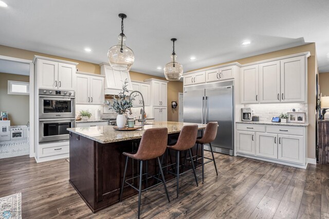 kitchen featuring dark wood-style flooring, an island with sink, recessed lighting, tasteful backsplash, and appliances with stainless steel finishes