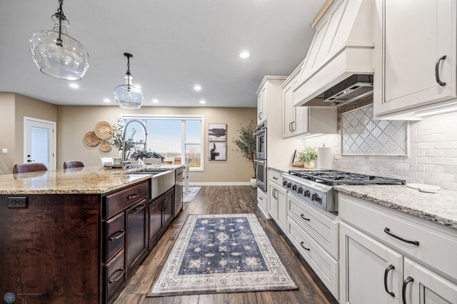 kitchen with white cabinets, dark brown cabinets, an island with sink, stainless steel appliances, and custom range hood