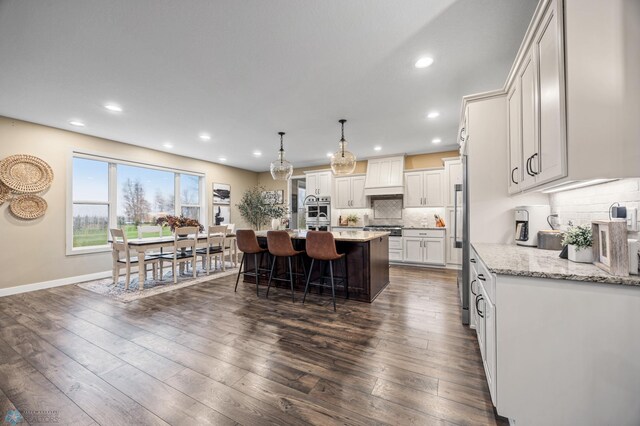 kitchen with decorative backsplash, a kitchen island with sink, a kitchen bar, dark wood finished floors, and recessed lighting