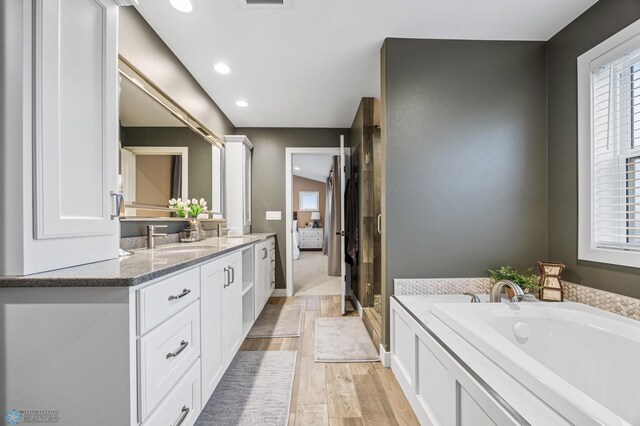 bathroom featuring a sink, double vanity, recessed lighting, wood finished floors, and a bath