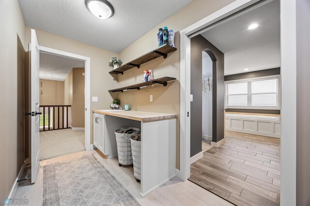 interior space with arched walkways, baseboards, a textured ceiling, and light wood-type flooring