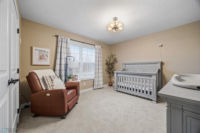 bedroom featuring a textured ceiling, a nursery area, baseboards, an inviting chandelier, and light carpet