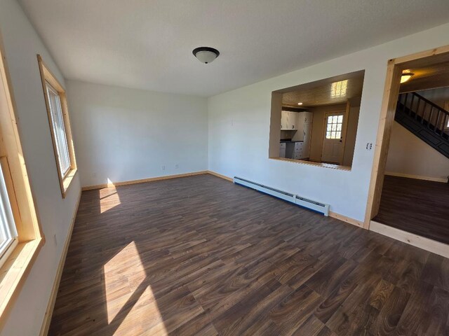 empty room featuring stairs, dark wood-style flooring, baseboards, and a baseboard heating unit