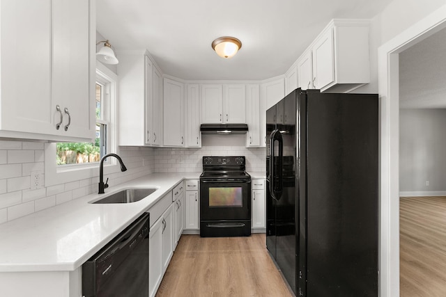 kitchen featuring a sink, black appliances, light wood-type flooring, and under cabinet range hood