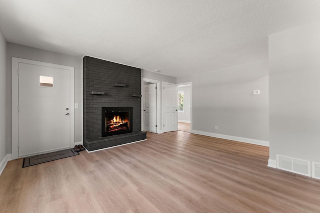 unfurnished living room with baseboards, a brick fireplace, light wood-type flooring, and visible vents