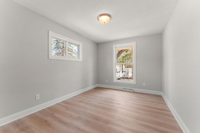 spare room featuring baseboards, light wood-type flooring, a textured ceiling, and visible vents