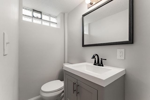 half bathroom featuring vanity, a textured ceiling, and toilet
