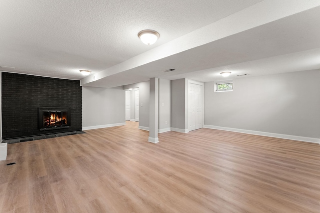 below grade area with visible vents, a fireplace, baseboards, a textured ceiling, and light wood finished floors