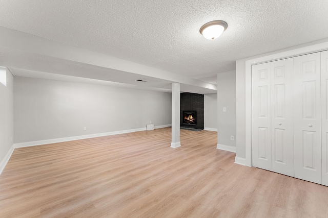 below grade area featuring a fireplace, a textured ceiling, baseboards, and light wood-style floors