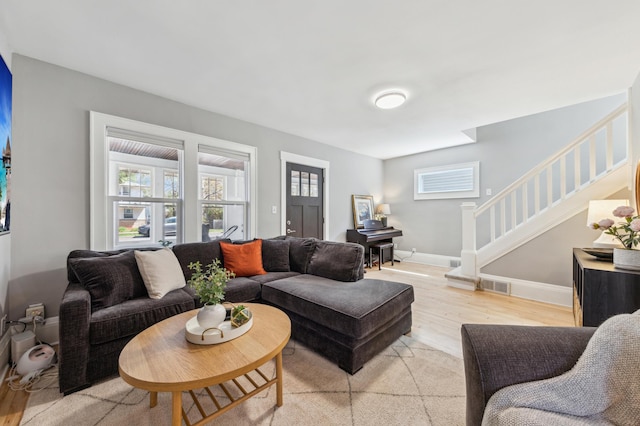 living room with baseboards, stairway, light wood-style flooring, and visible vents