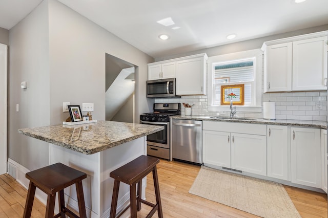kitchen with a breakfast bar area, a sink, white cabinetry, light wood-style floors, and appliances with stainless steel finishes