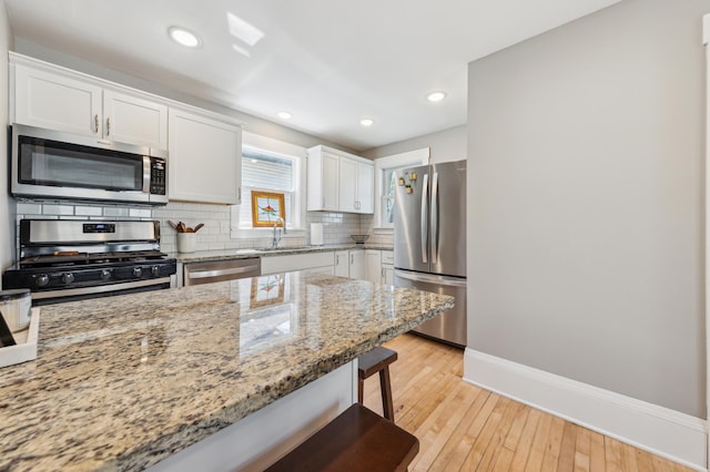 kitchen with baseboards, backsplash, light wood-style floors, white cabinets, and appliances with stainless steel finishes