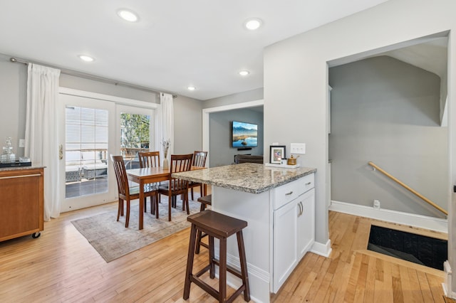 kitchen with light wood finished floors, a kitchen breakfast bar, light stone countertops, and recessed lighting