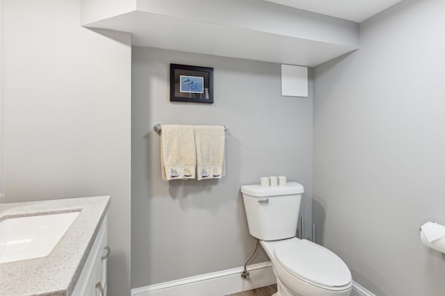 half bath with toilet, baseboards, vanity, and wood finished floors