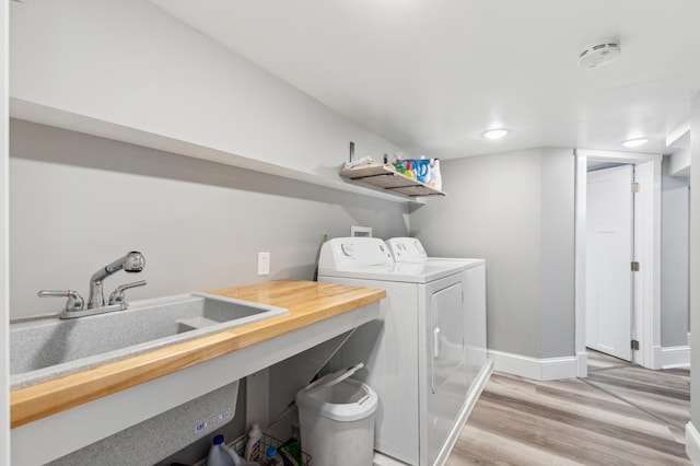 laundry area featuring a sink, laundry area, washing machine and dryer, baseboards, and light wood-style floors
