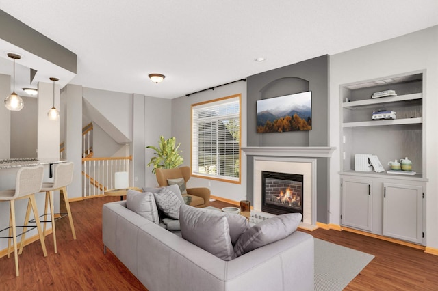 living area with wood finished floors, a glass covered fireplace, baseboards, built in shelves, and stairway